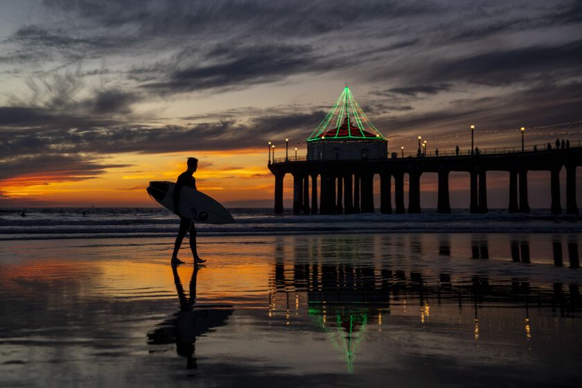 Manhattan Beach, CA - December 21: Surfers are silohuetted, as the sun sets and the Christmas lights twinkle on the Manhattan Beach Pier in Manhattan Beach, CA, Tuesday, Dec. 21, 2021. (Jay L. Clendenin / Los Angeles Times)