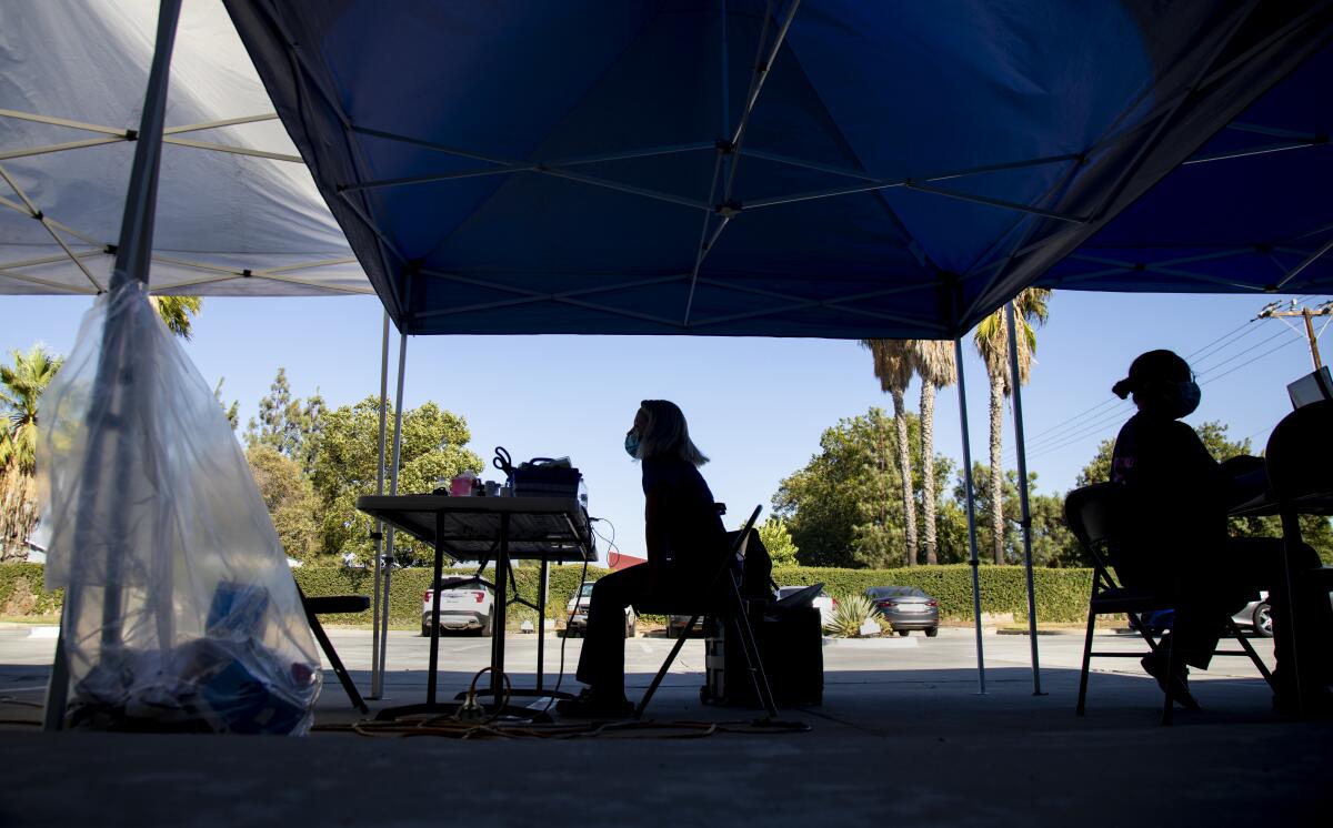 Nurses wait in a parking lot under tents