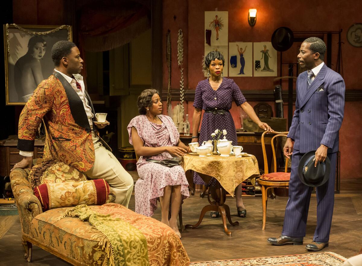 Two men and two women in period clothing on a stage set of a period living room.