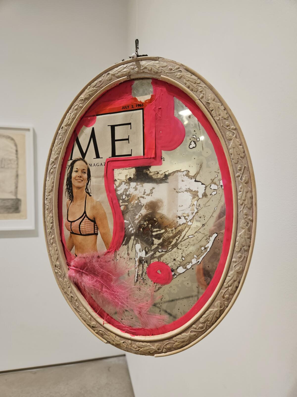 A fragment of a Time magazine cover with the “TI” clipped off, showing a woman in a bikini, pasted on an oval mirror.