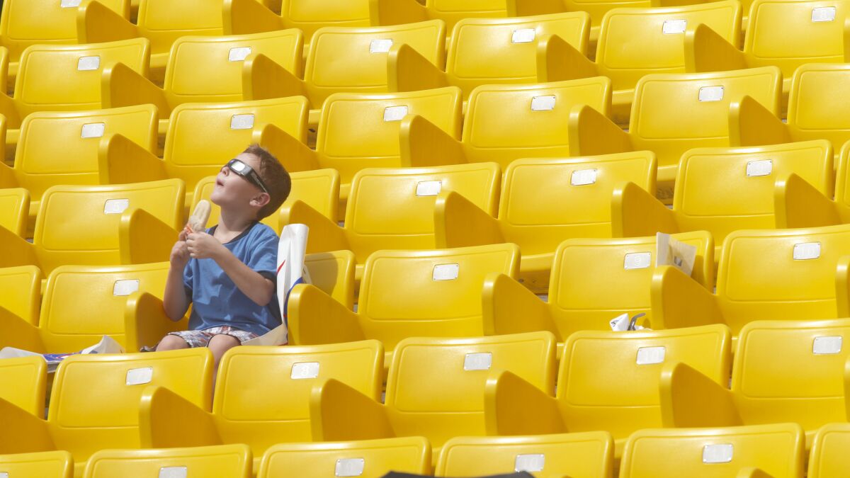 A boy sitting in a section of bright yellow stadium seats looks up toward the sky while holding a popsicle.