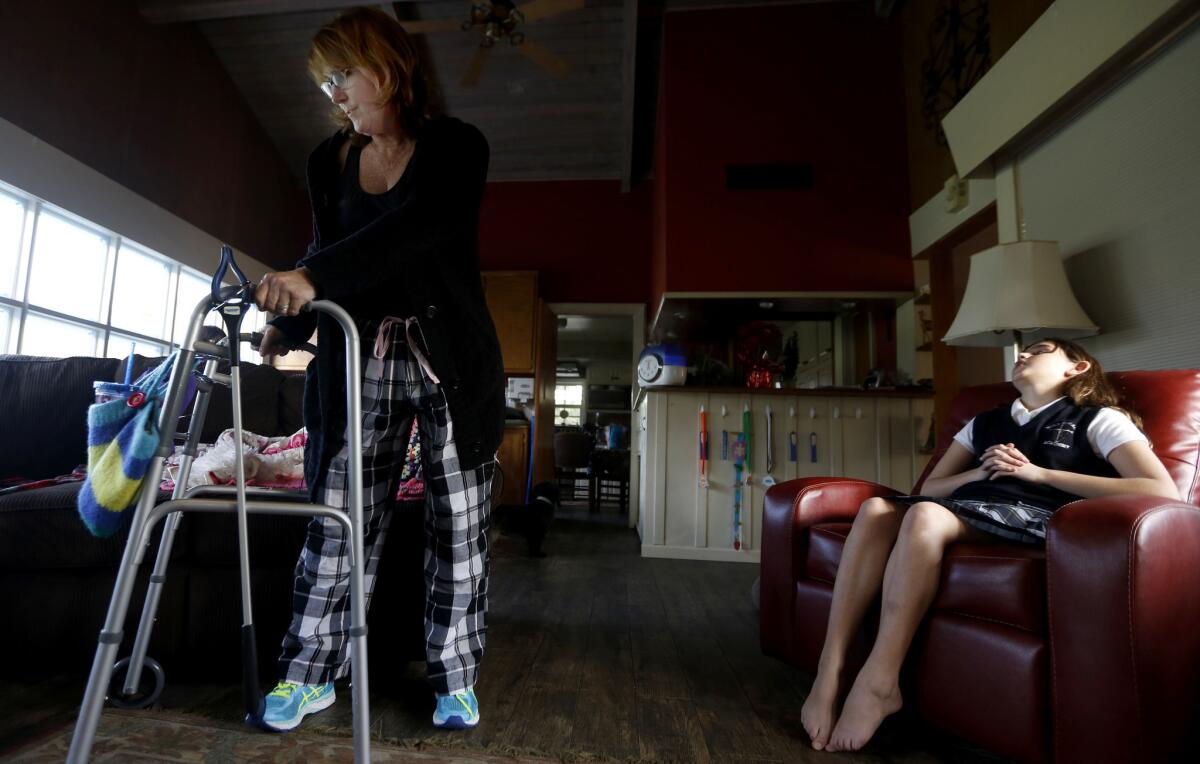 Julie Swann-Paez, shot in the pelvis in the Dec. 2 attack at the Inland Regional Center, uses a walker to move around her living room. She takes Tylenol to endure the pain and a muscle relaxant to sleep through the night. At right is her daughter Ellie, 11.
