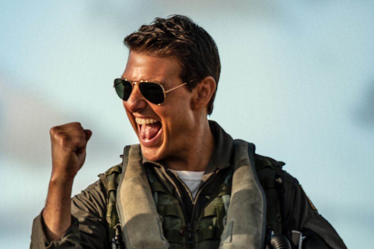 Tom Cruise wearing sunglasses, smiling and raising a fist
