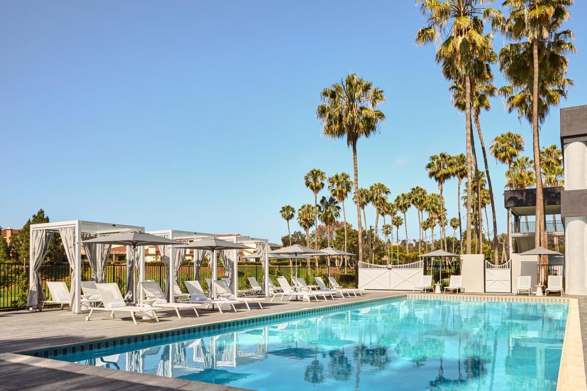 The Westdrift Manhattan Beach pool with a line of covered lounge chairs and palm trees