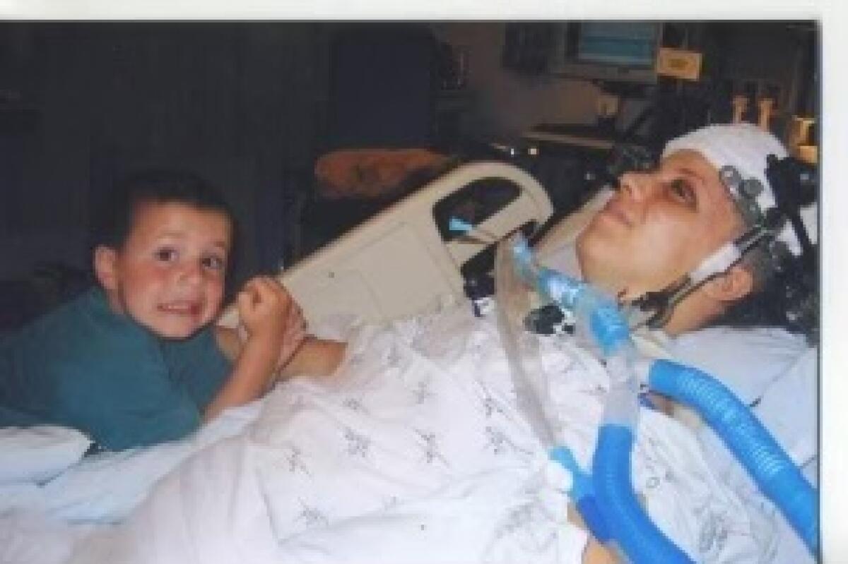 Erica Predum holds her son's hand while lying in a hospital bed after a traumatic spinal cord injury.