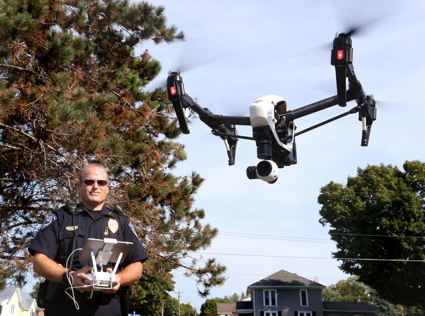 A man in police uniform holds a controller while a drone hovers nearby 