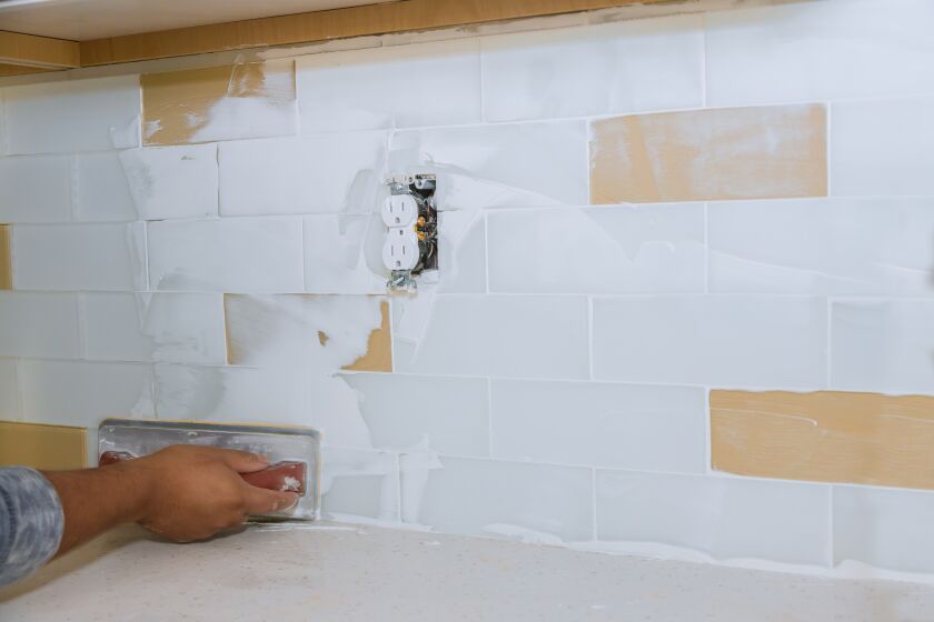 A person applies grout to new backsplash tiles in a kitchen renovation.