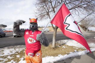 FILE - A Kansas City Chiefs fan, Chiefsaholic, poses for photos while walking toward Empower Field at Mile High before an NFL football game between the Denver Broncos and the Chiefs, Jan. 8, 2022, in Denver. An Oklahoma judge has ordered the Kansas City Chiefs superfan known as “ChiefsAholic” who admitted to a series of bank robberies to pay $10.8 million to a bank teller he threatened and assaulted with a gun. (AP Photo/David Zalubowski, file)