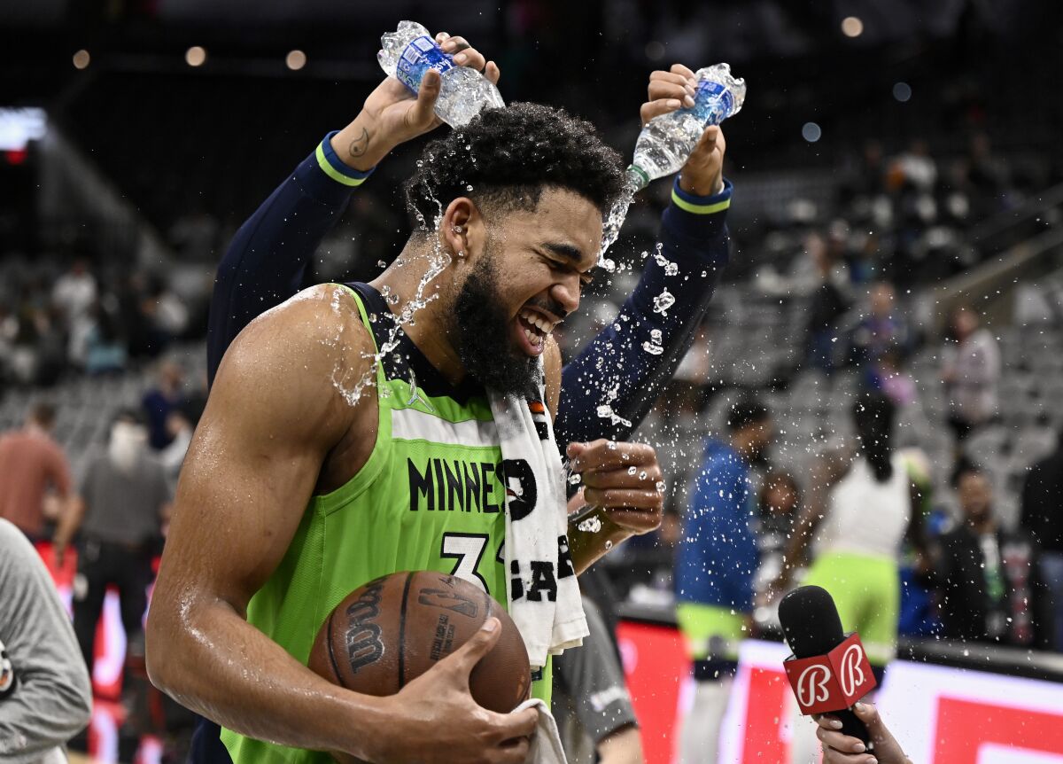 Minnesota Timberwolves center Karl-Anthony Towns is doused by teammate D'Angelo Russell, rear, after an NBA basketball game against the San Antonio Spurs on Monday, March 14, 2022, in San Antonio. (AP Photo/Darren Abate)