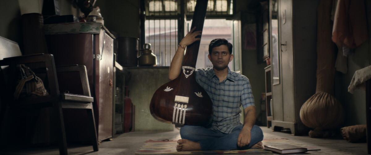 A man holding an instrument sits cross-legged