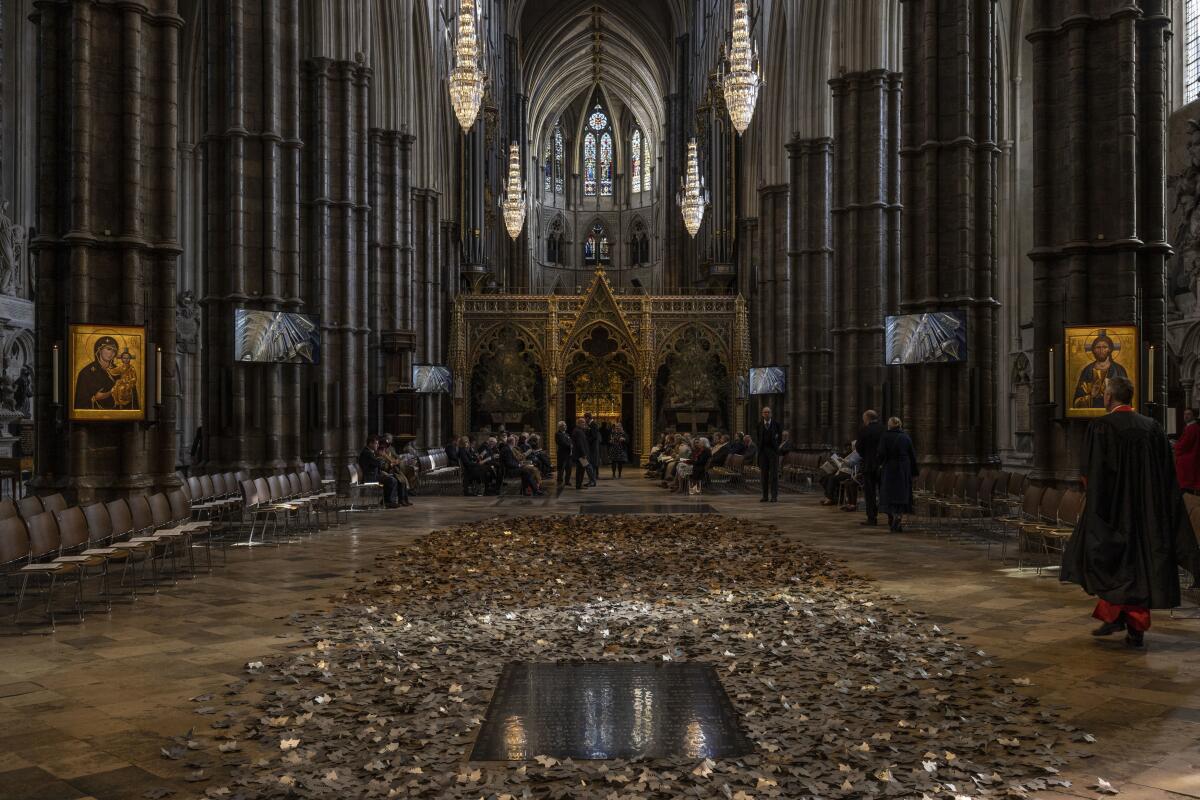 Metal leaves are seen on the ground in the middle of a church building with a soaring ceiling and chandeliers.