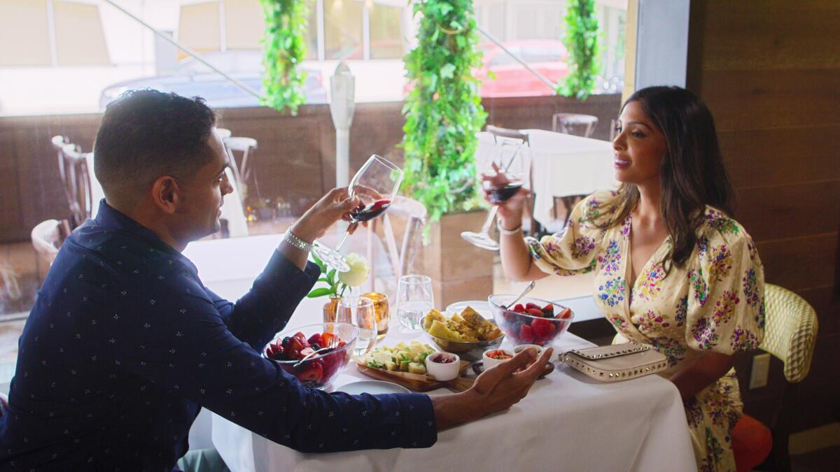 A man and woman sitting across from each other raise their glasses at a sunlit restaurant.