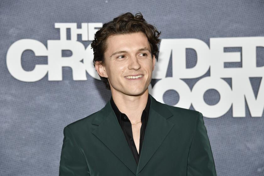 Tom Holland smiles in a green suit against a gray background.