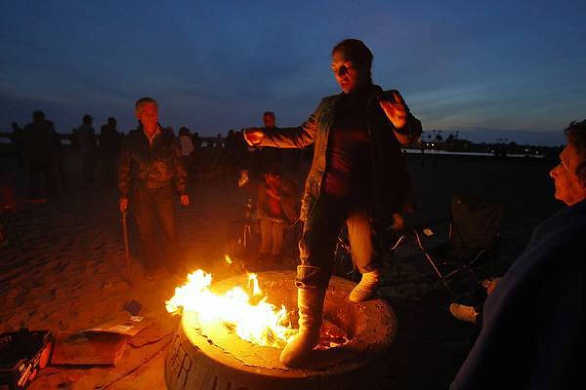 Zenya Shir of Irvine jumps over a fire pit at Corona Del Mar State Beach in March. Such wood-fueled fire rings may be replaced by natural gas rings if Newport Beach approves a pilot program with the South Coast Air Quality Management District.