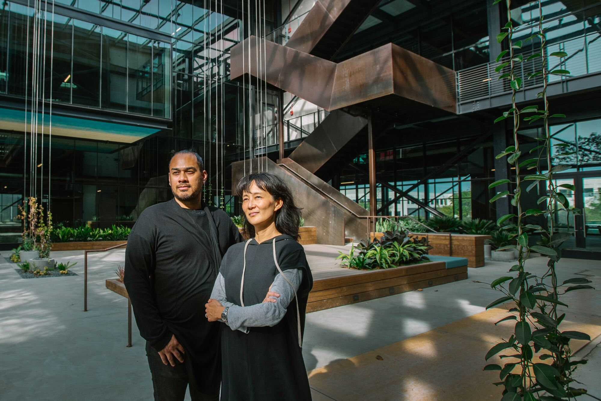 George Racomura and Patricia Rhee are seen standing in the atrium at the Press, before a staircase wrapped in Cor-Ten steel