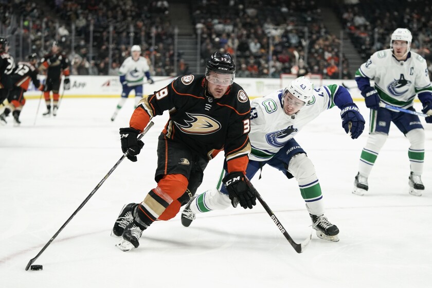 Anaheim Ducks' Sam Carrick, left, moves the puck past Vancouver Canucks' Quinn Hughes.