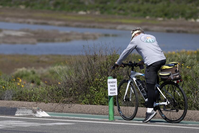San Diego CA - March 20: A cyclist stops to remove a sign on the east side of South Coast Highway across from the Cardiff State Beach parking lot in Encinitas on Wednesday, March 20, 2024. The sign said remove these killer posts. Early Sunday, a man died after a crash here where there is a pylon and raised curb separating the bike lane and vehicle lanes. Bicyclists are also allowed to ride in the vehicle lanes. (K.C. Alfred / The San Diego Union-Tribune)