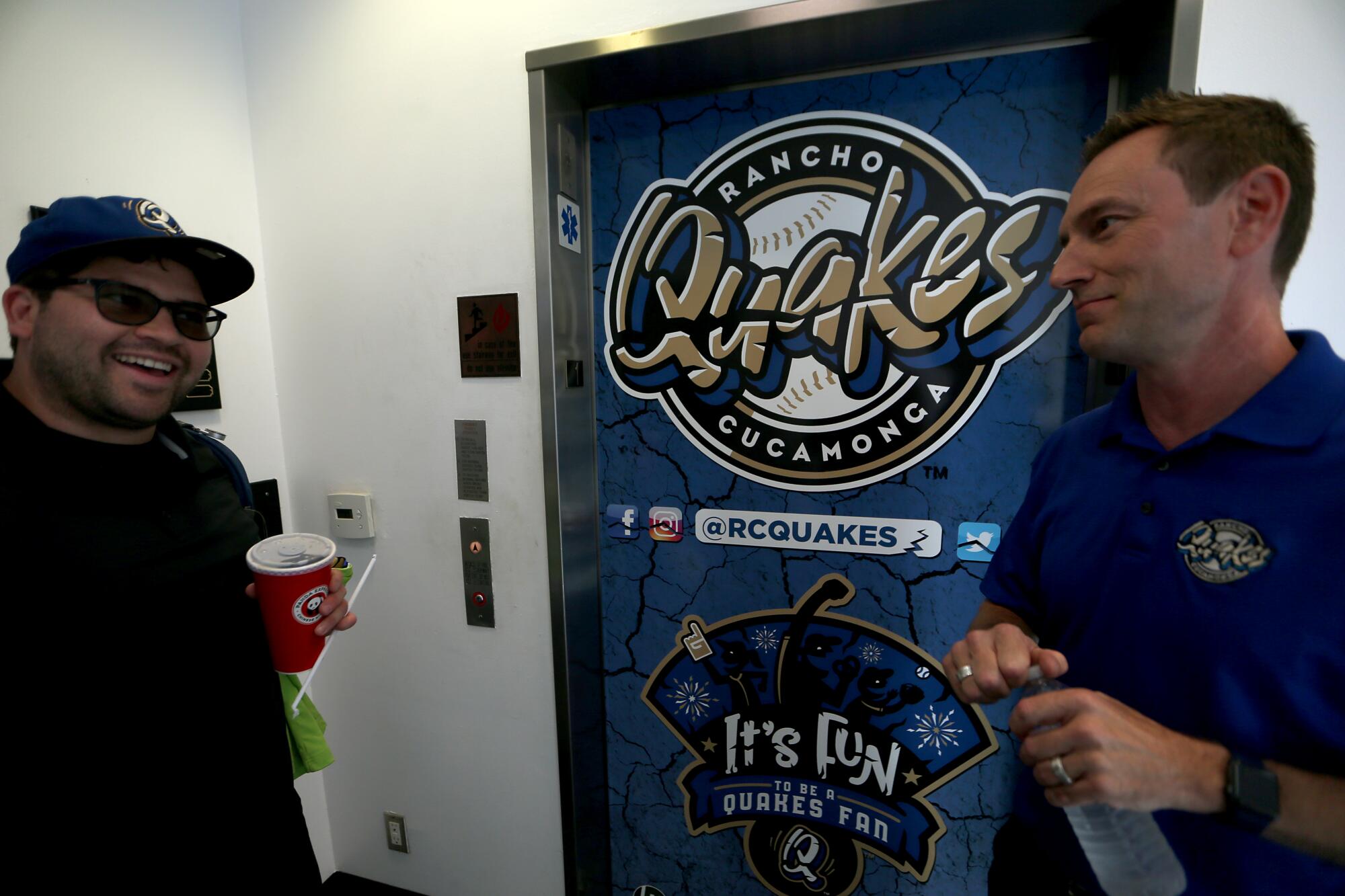 İki adam Rancho Cucamonga Quakes logosunun önünde konuşuyor