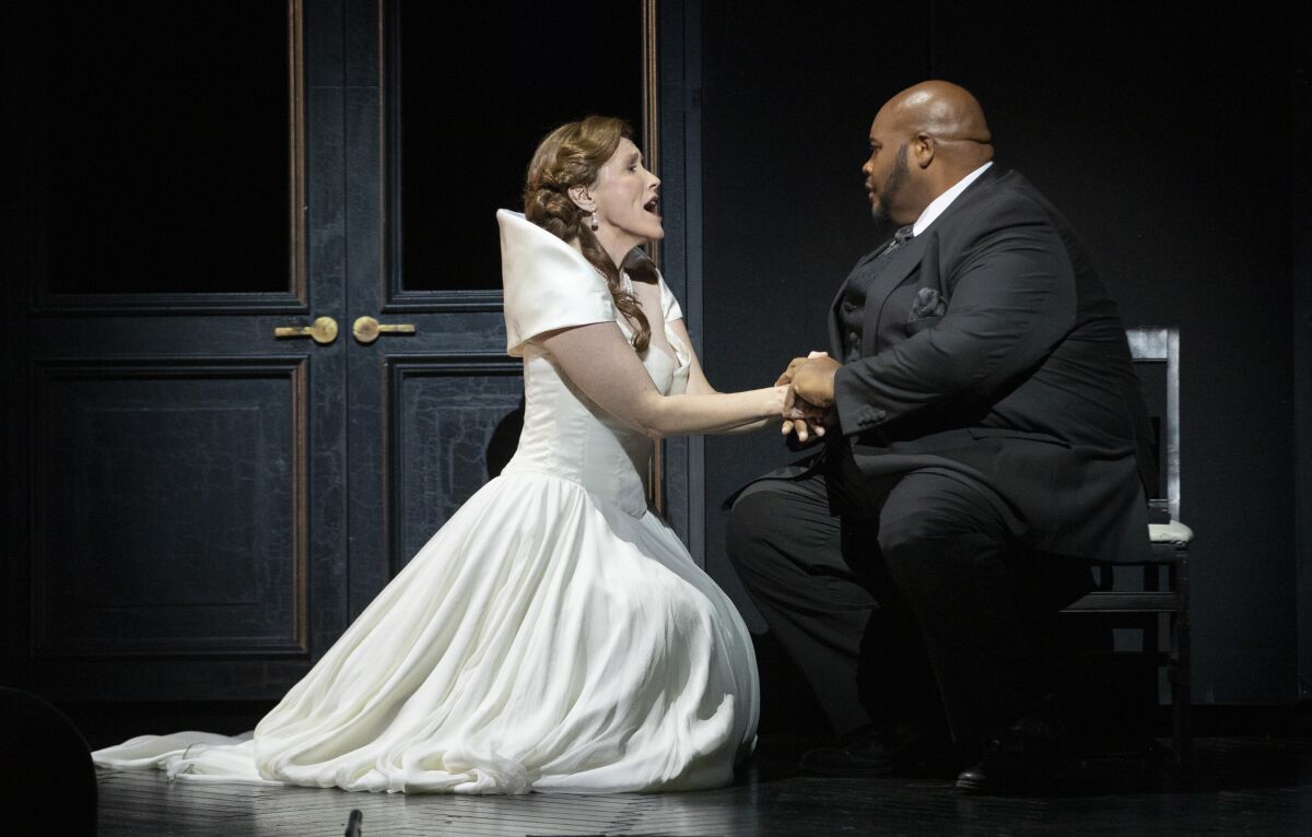 A woman in a white gown sings passionately while holding the hands of a man in a tux