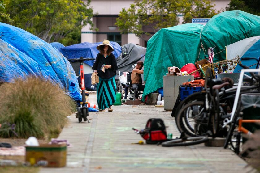 VENICE, CA - MAY 23: A woman walks down the long row of tents at the homeless encampment outside Abbot Kinney Memorial Branch Library on Monday, May 23, 2022 in Venice, CA. (Jason Armond / Los Angeles Times)