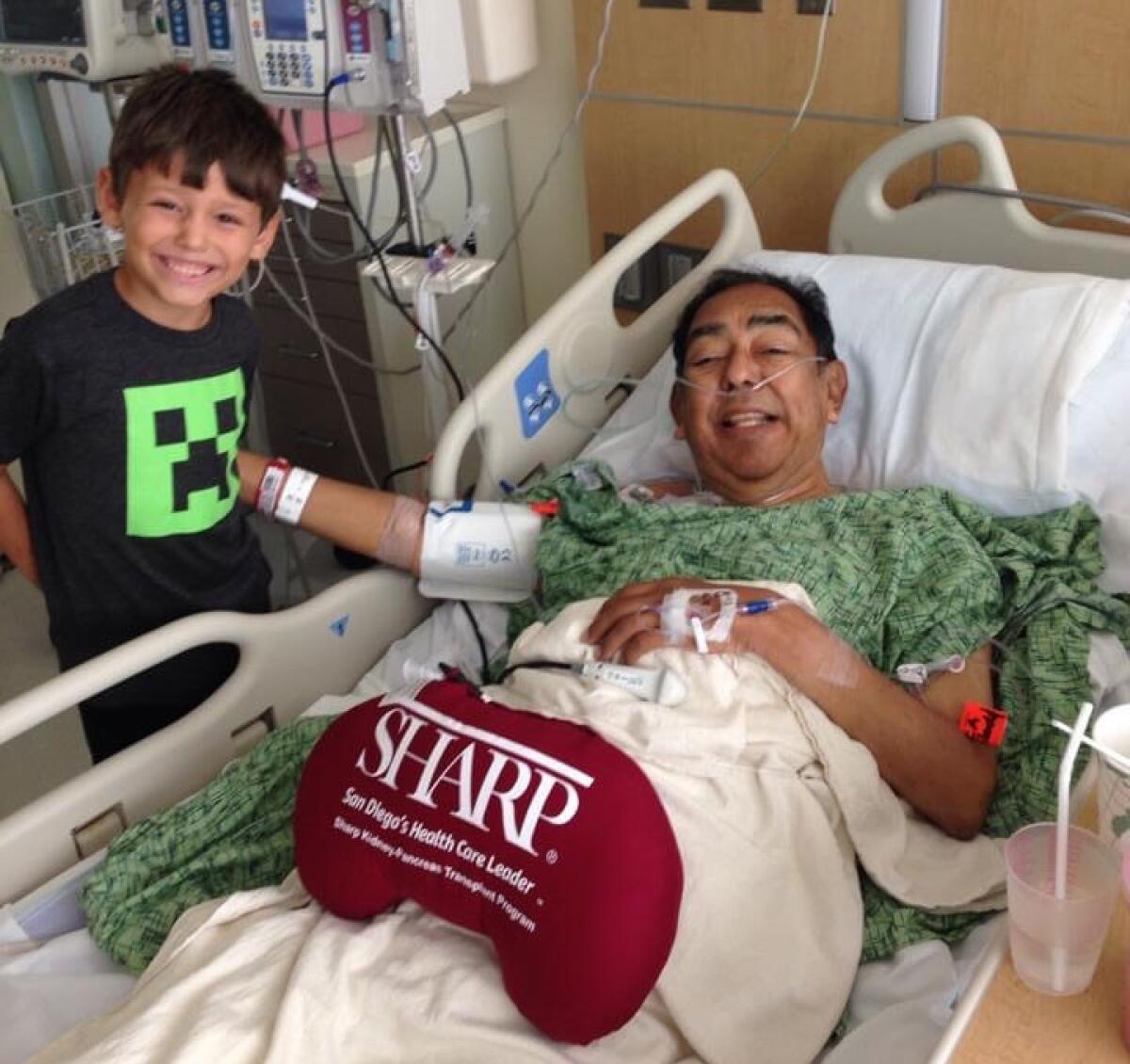 Macias in a hospital bed with his young grandson standing next to him.