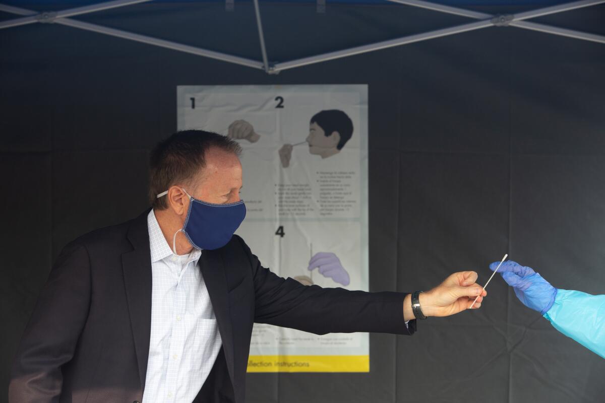 Austin Beutner, in mask, places a swab in the gloved hand of a health worker.