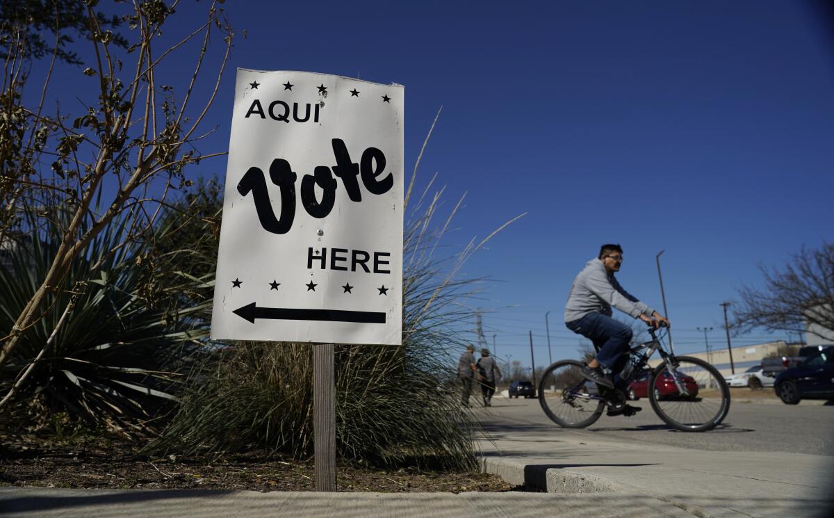 A man on a bicycle passes a "Vote here" sign