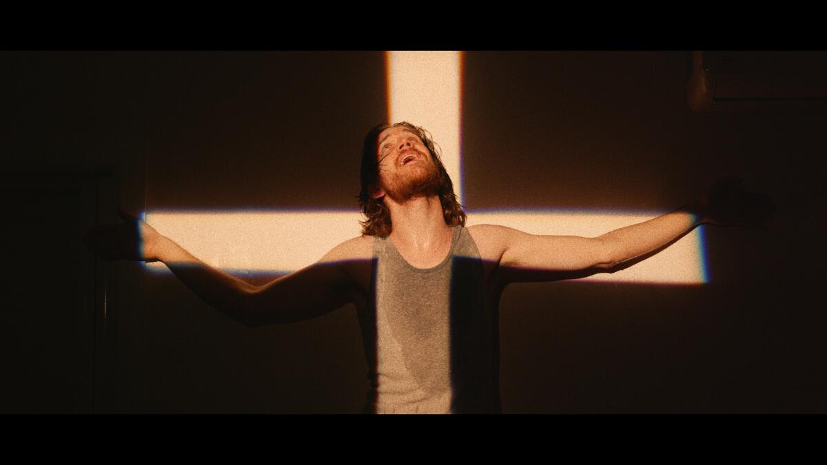 Bo Burnham appears as a Christ-like figure in light and shadows creating the shape of a cross.