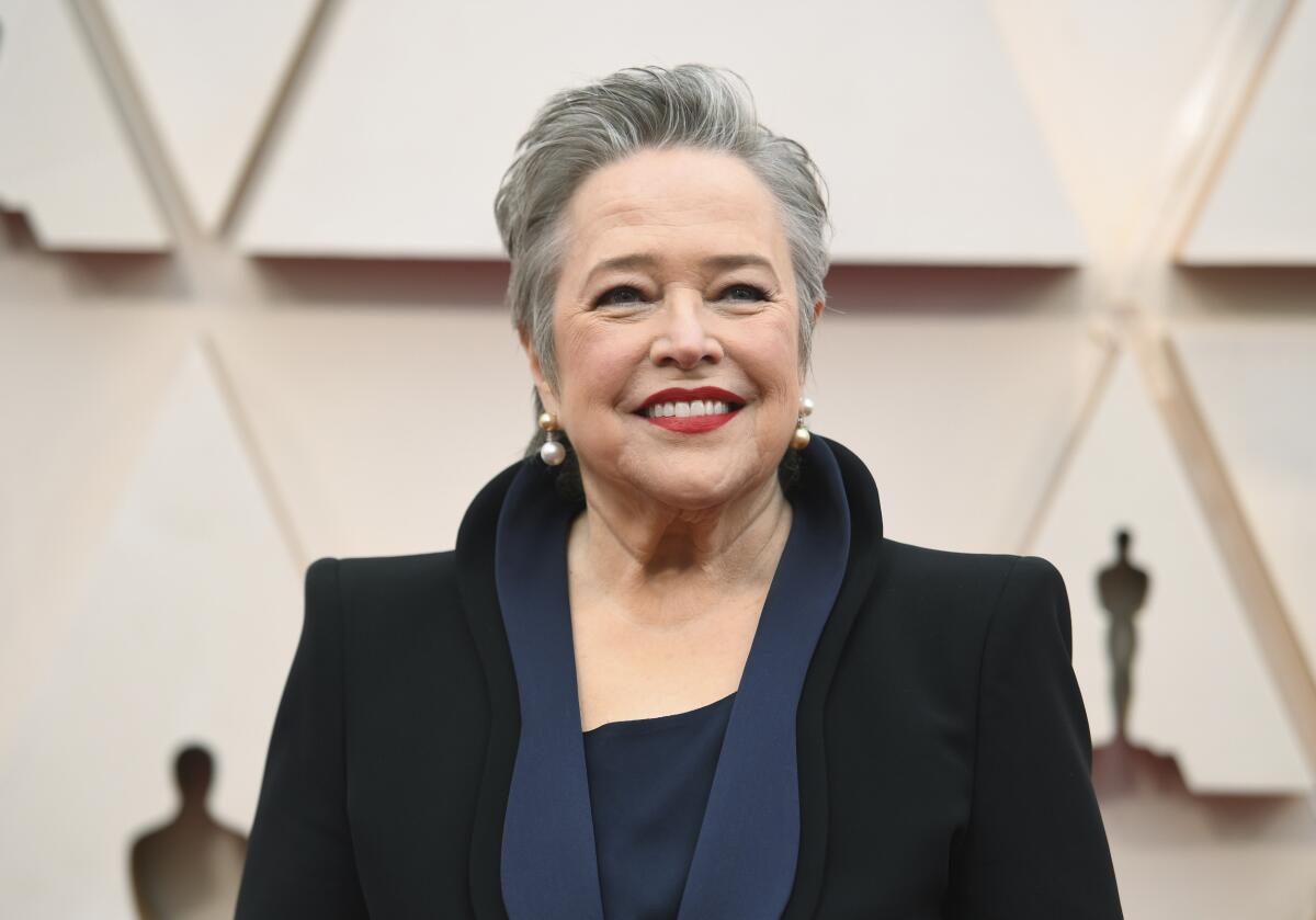 Kathy Bates smiling in a black dress with a high collar and wide shoulders