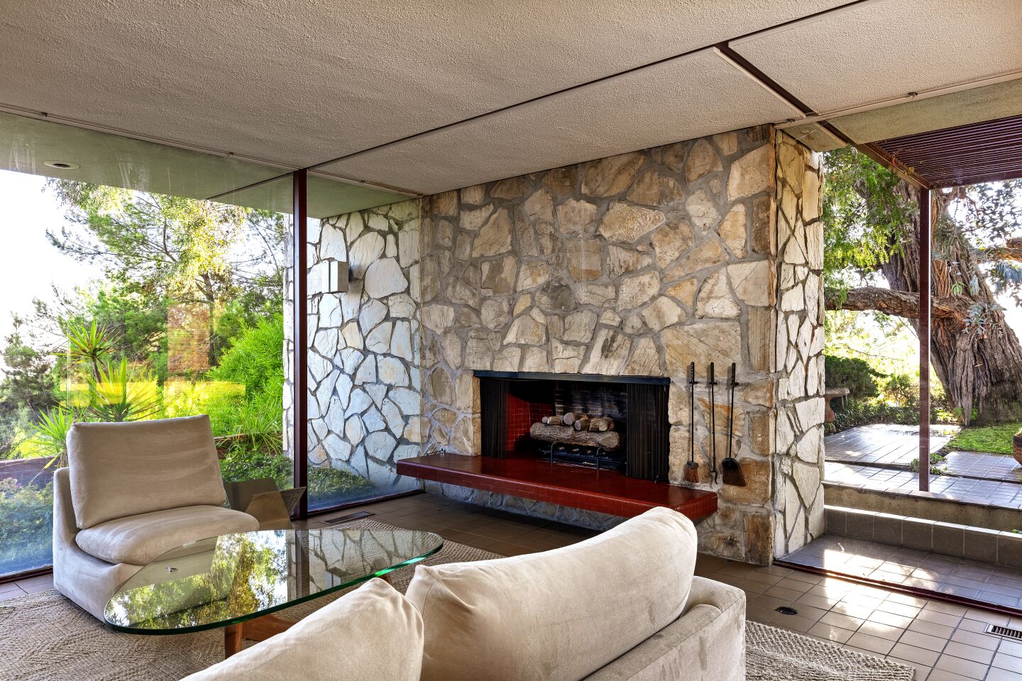 The living room’s Palos Verde stone-clad fireplace continues through the glass creating a second outdoor patio hearth anchored by three ancient eucalyptus.