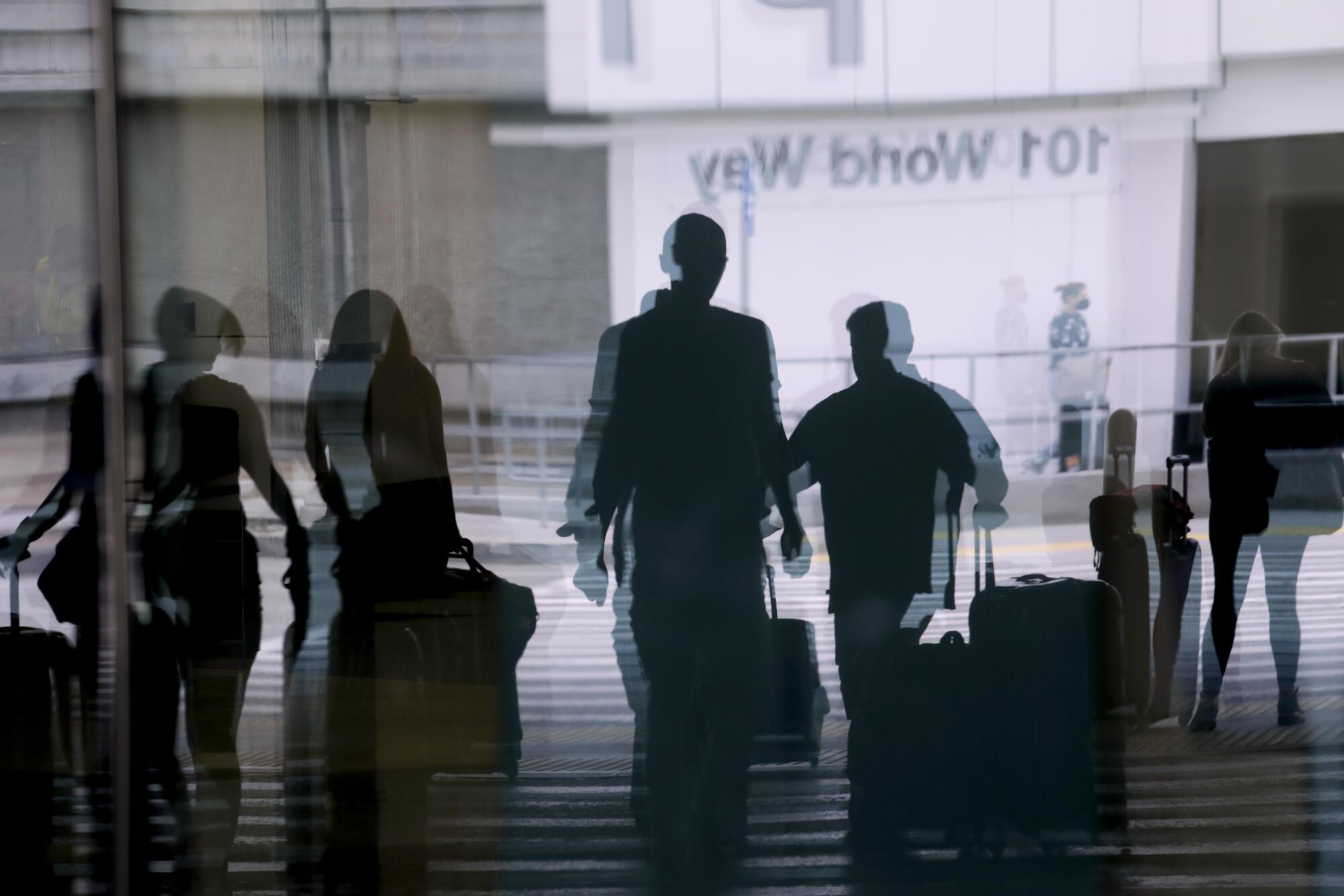 Travelers, caught in a reflection, begin their Memorial Day holiday getaway at the Los Angeles International Airport.