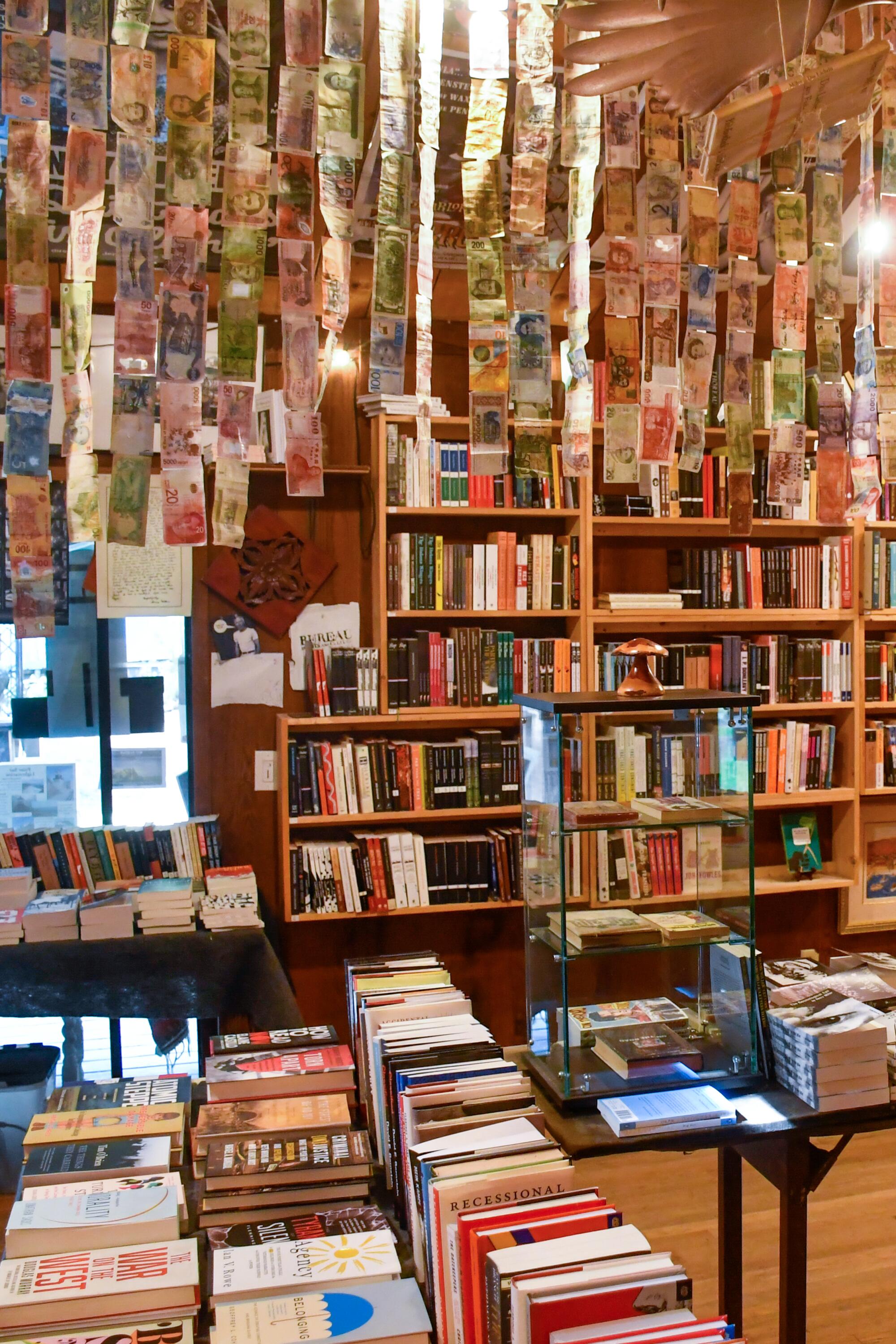 The inside of a library, with books stacked everywhere and foreign currency hanging in streamers from the ceiling.