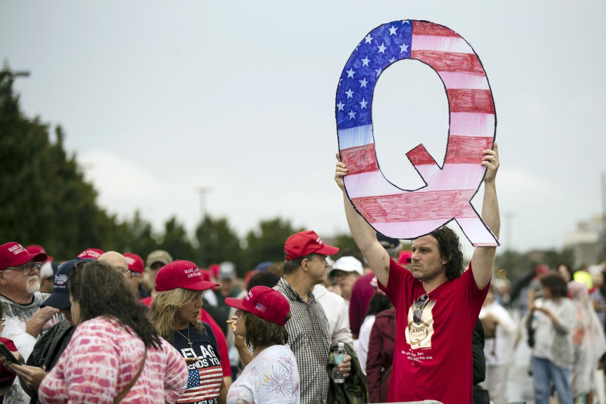 A person holds a sign in the shape of the letter Q colored like the U.S. flag outside a Trump campaign rally