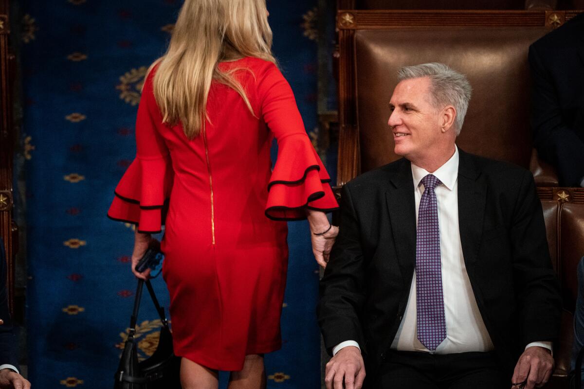 A woman in a red dress walks by a man in a suit and tie 