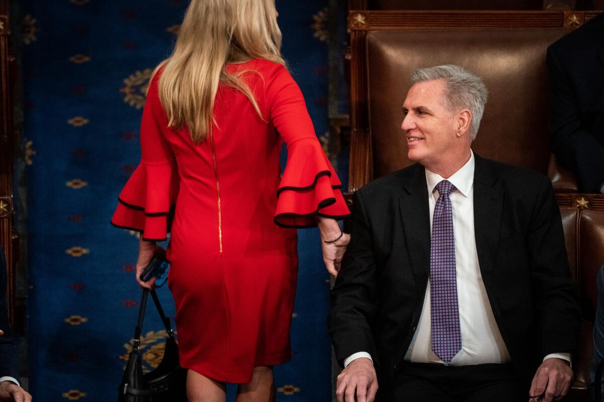 A woman in a red dress walks by a man in a suit and tie