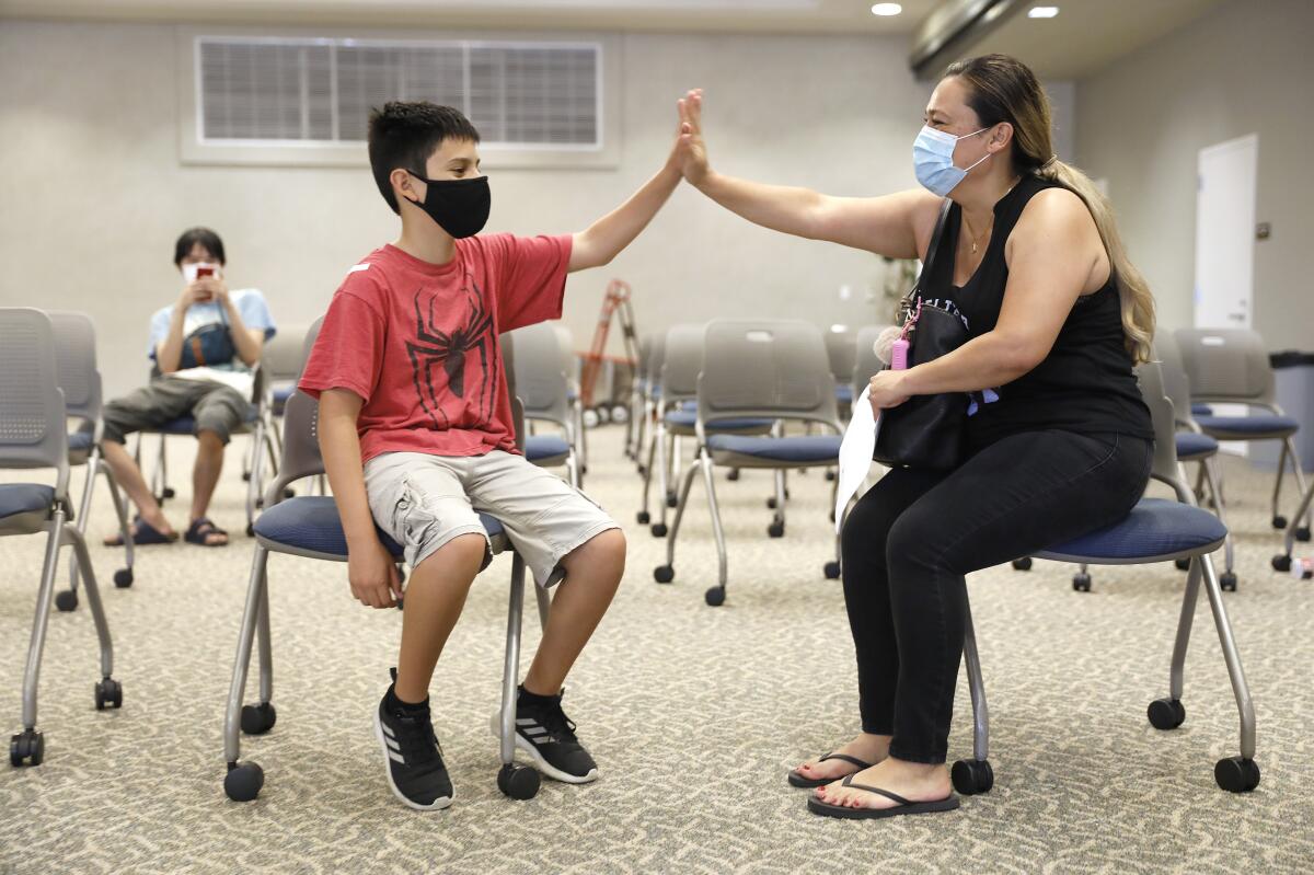 A boy and a woman wearing masks high-five while seated in folding chairs.