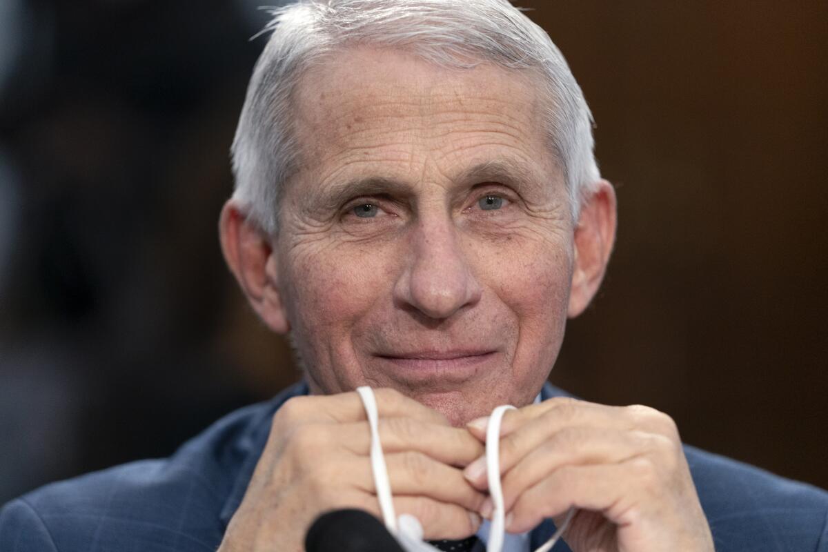 Dr. Anthony Fauci holding a face mask in his hands and smiling.
