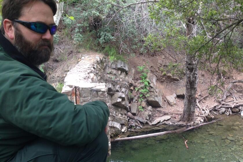 Darrell Vance of the U.S. Forest Service crouches along a bank overlooking a vintage dam and swimming hole in Orange County's Silverado Canyon, which is scheduled for demolition.