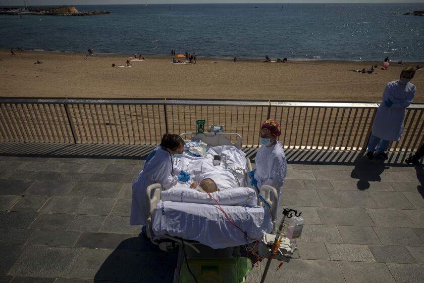 Francisco España, 60, is surrounded by members of his medical team as he looks at the Mediterranean sea from a promenade next to the "Hospital del Mar" in Barcelona, Spain, Friday, Sept. 4, 2020. A hospital in Barcelona is studying how short trips to the beach may help COVID-19 patients recover from long and traumatic intensive hospital care. The study is part of a program to “humanize” ICUs. Since re-starting it in early June, the researchers have anecdotally noticed that even ten minutes in front of the blue sea waters can improve a patient’s emotional attitude. (AP Photo/Emilio Morenatti)