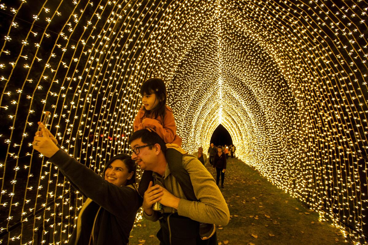 A family of three pose for a selfie under a peaked tunnel of cascading white lights