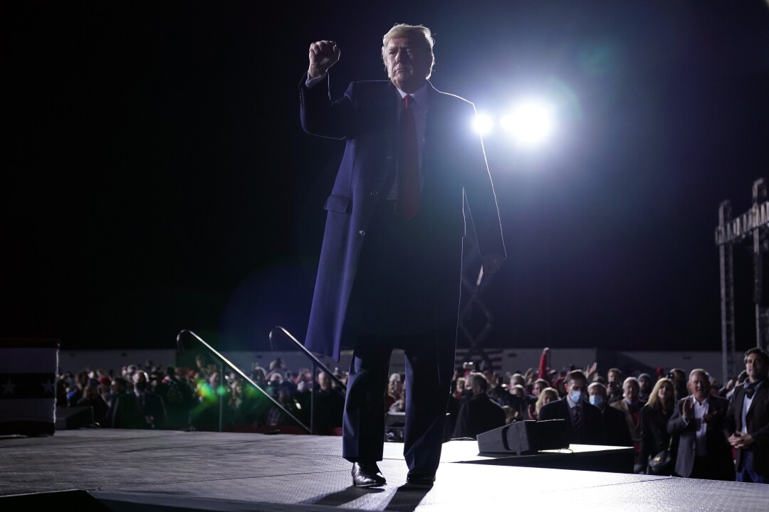 President Trump, in suit and overcoat, raises a fist on stage.