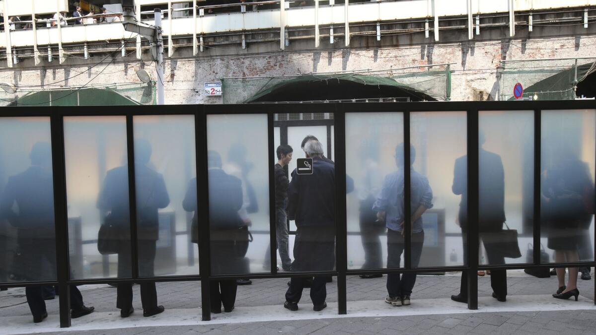 Smokers crowd designated smoking area in Tokyo.