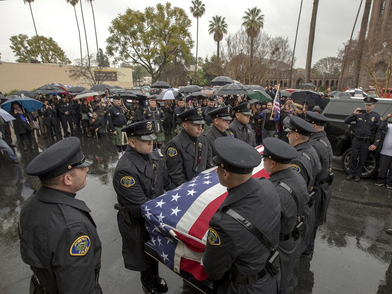 People stand in rain as Pomona Police Officer Greggory Casillas's funeral procession leaves Purpose Church for internment.