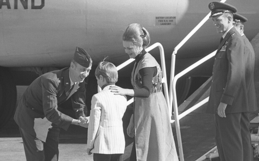 A man shakes the hand of a young boy as a woman and two men in uniform look on.