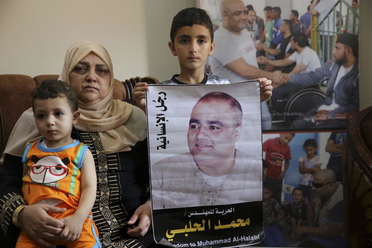 FILE - Amal el-Halabi holds her grandson Fares while her grandson Amro, 7, holds a picture of his father Mohammed el-Halabi, Gaza director of the international charity World Vision, who is detained and accused by Israeli security of diverting sums to Hamas that exceed its total budget, at his family house in Gaza City, Aug. 8, 2016. In May 2022, nearly six years after Israel accused Mohammed el-Halabi of diverting tens of millions of dollars from an international charity to Gaza's militant Hamas rulers, he has yet to be convicted in an Israeli court and is still being held in detention. World Vision as well as independent auditors and the Australian government, have found no evidence of any wrongdoing. Arabic on the picture reads, " the man of humanity." (AP Photo/Adel Hana, File)