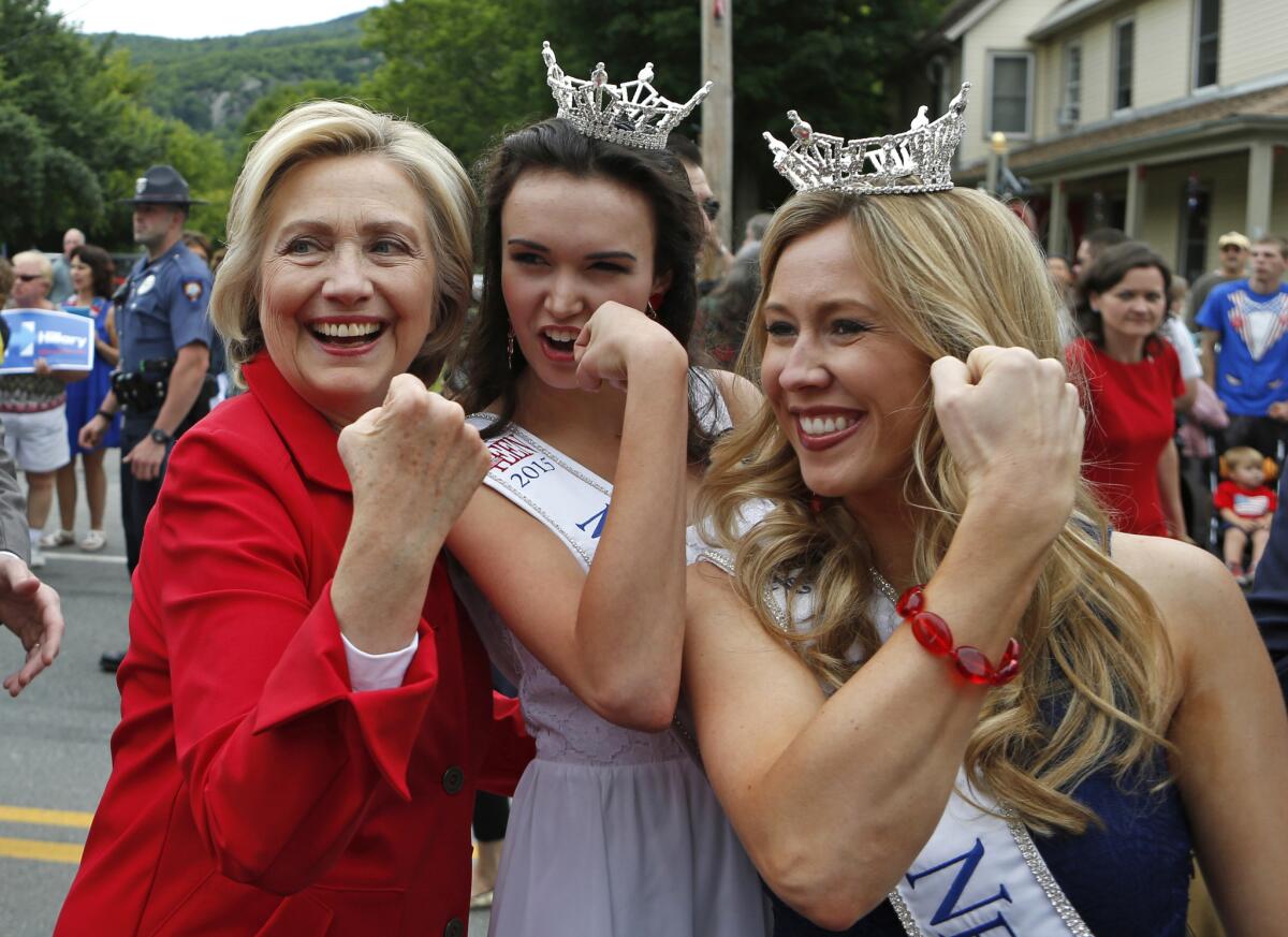 La candidata presidencial Hillary Rodham Clinton, flexiona sus músculos junto con Miss Teen New Hampshire, Allie Knault, al centro, y Miss New Hampshire, Holly Blanchard,durante un desfile del 4 de Julio en Gorham, Nueva Hampshire el 4 de julio de 2015. (Foto AP/Robert F. Bukaty)