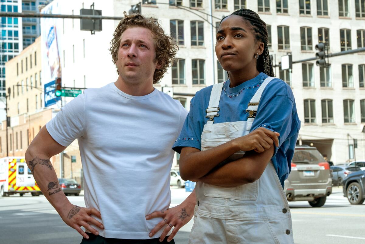 Jeremy Allen White and Ayo Edebiri stand on the street looking intensely at a building in "The Bear." 
