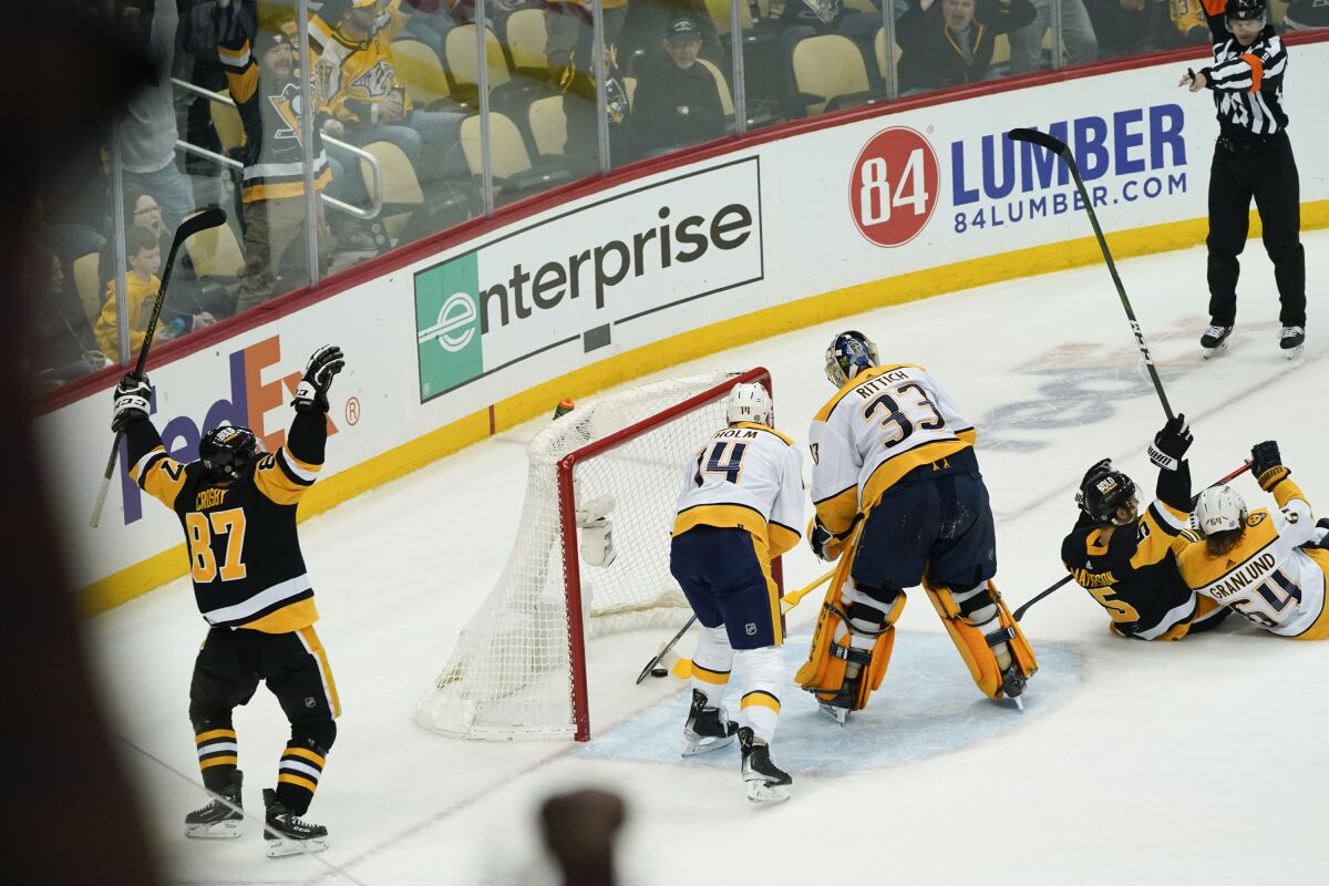 Pittsburgh Penguins' Sidney Crosby (87) celebrates after he scored as Nashville Predators' Mattias Ekholm, center, reaches for the puck behind goaltender David Rittich (33) during the overtime period of an NHL hockey game, Sunday, April 10, 2022, in Pittsburgh. The Penguins won 3-2. (AP Photo/Keith Srakocic)