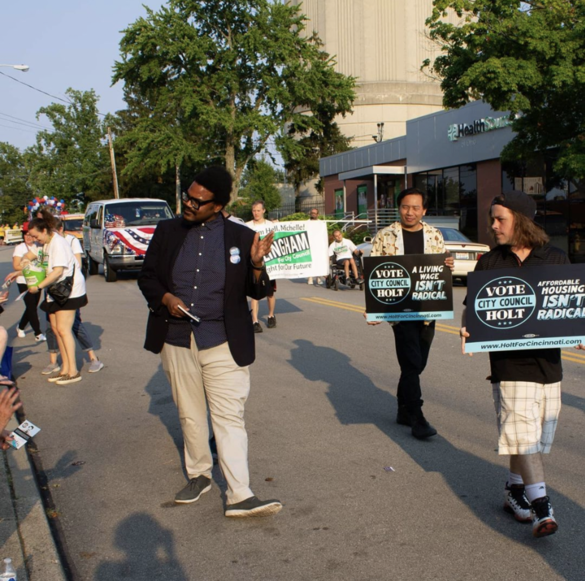 A person walks in the middle a street. People with signs walk next to him.