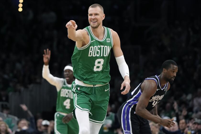 Kristaps Porzingis, de los Celtics de Boston, celebra un triple en la primera mitad del partido de la NBA ante los Kings de Sacramento, el viernes 5 de abril de 2024, en Boston. Al fondo, Hariso Barnes, de los Kings. (AP Foto/Michael Dwyer)